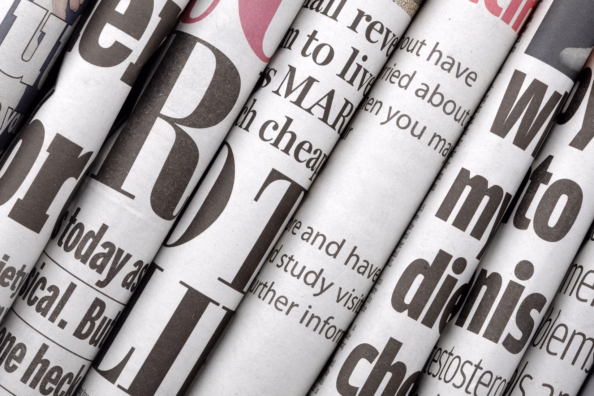 A close-up stack of rolled or layered daily newspapers featuring bold black and white typography and headlines.