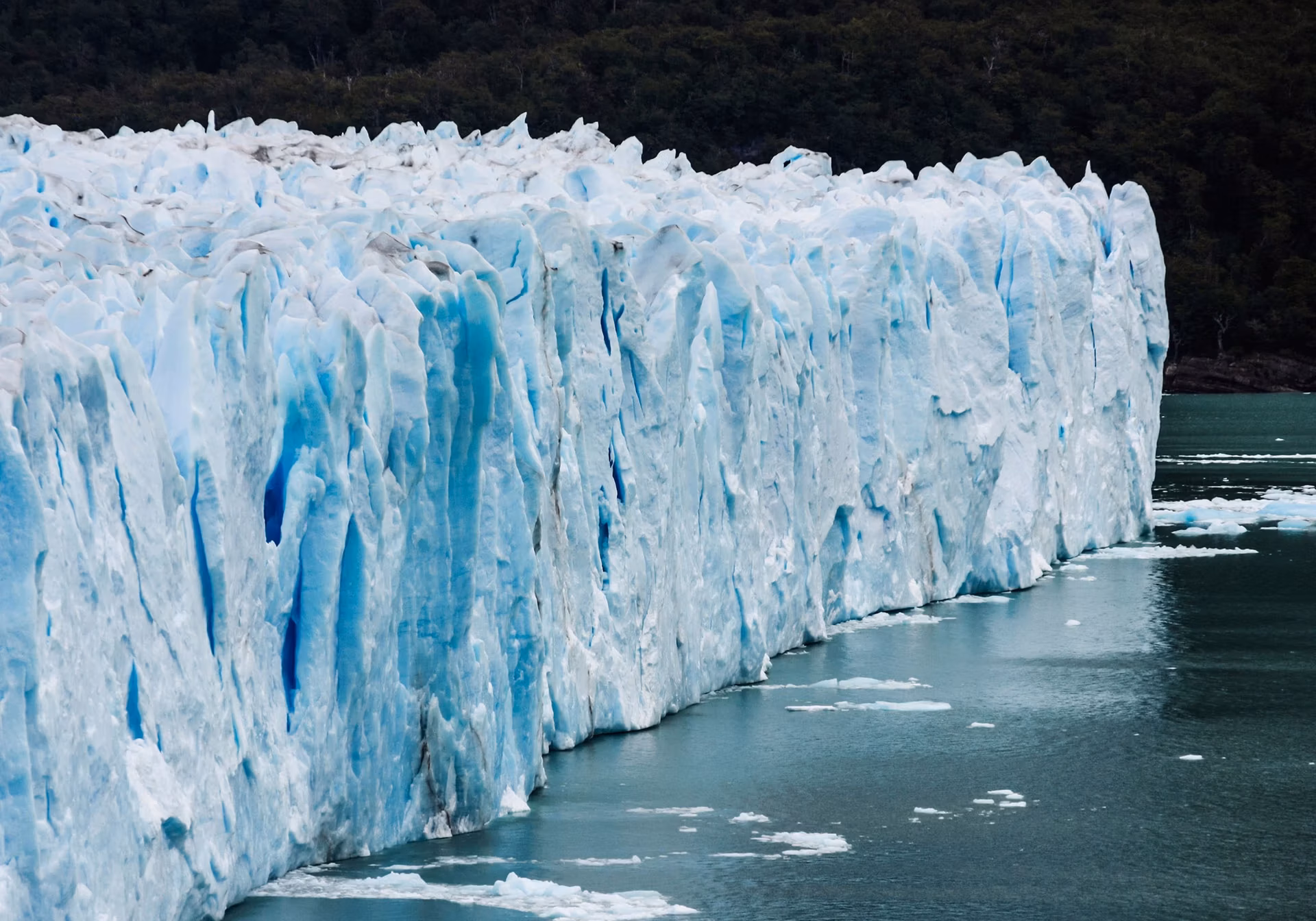 The towering, jagged face of a blue glacier meeting dark water filled with small ice fragments.