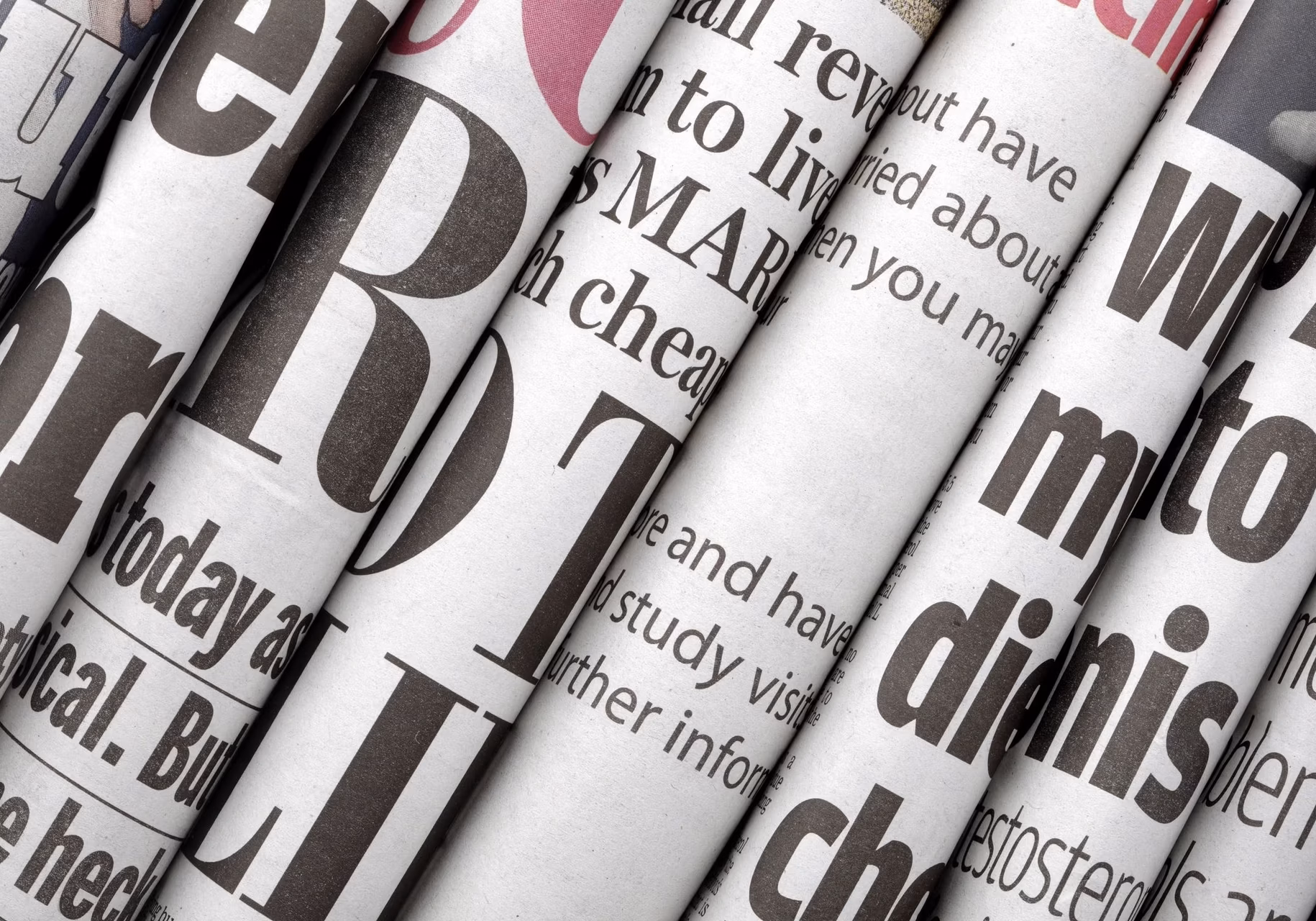A close-up stack of rolled or layered daily newspapers featuring bold black and white typography and headlines.